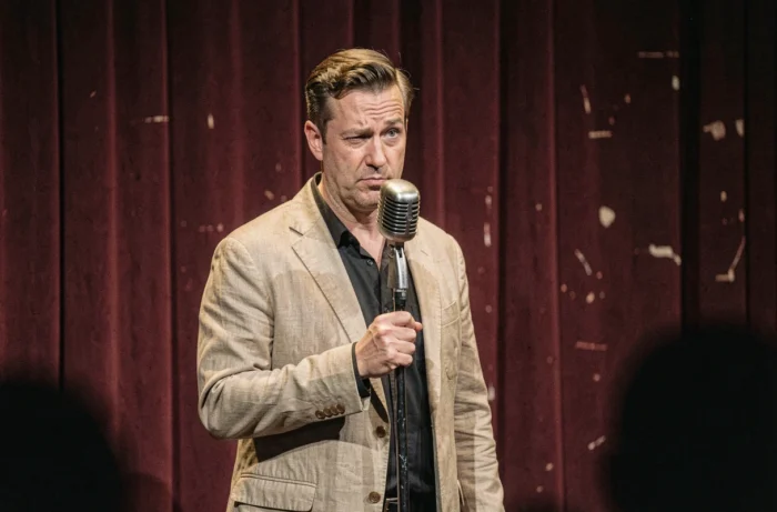 Comédien de stand-up en pleine performance sur scène avec expression pince-sans-rire, illustrant l'art de l'humour noir